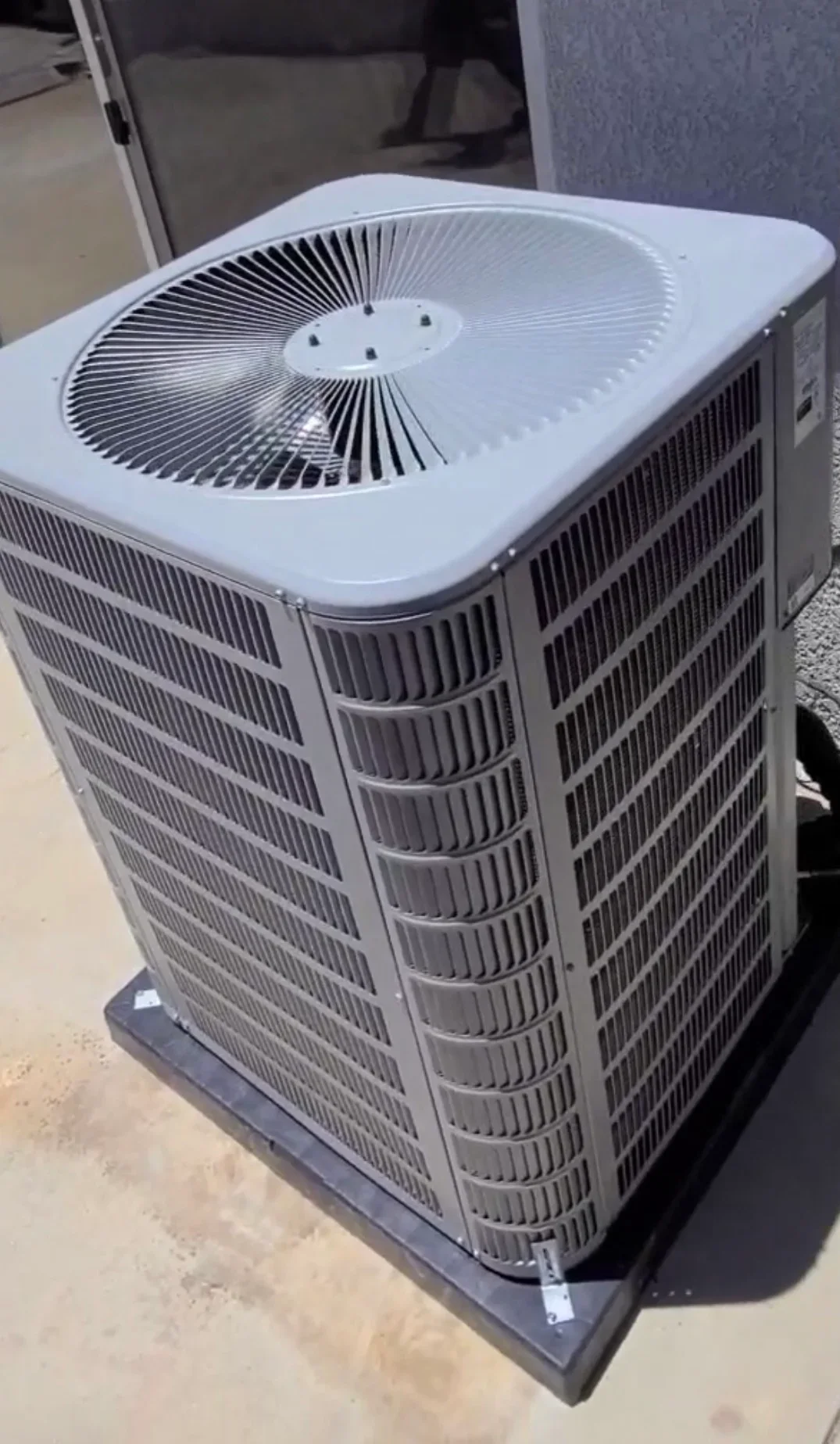White air conditioning condenser unit with fan assembly on concrete pad